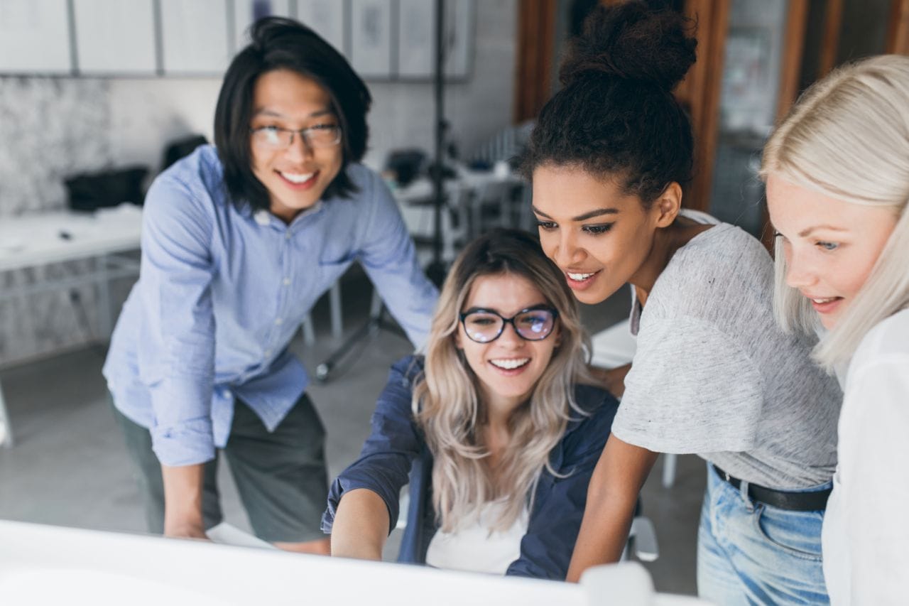 close up portrait of freelance it specialists looking at laptop screen with smile. asian programmer in glasses helping to mulatto girl in white t shirt with her project..