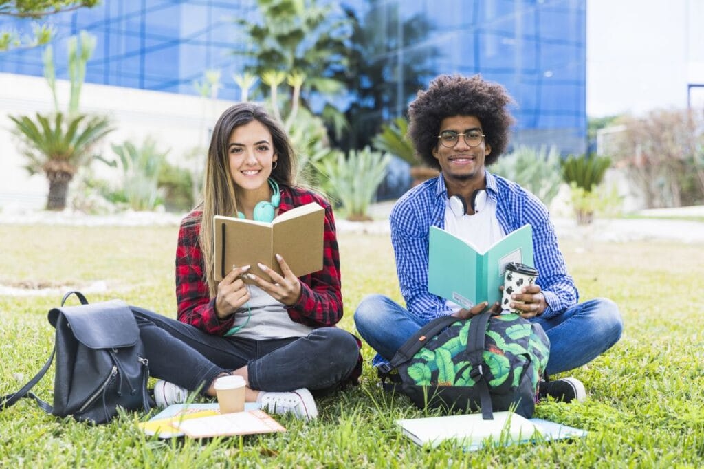diverse young couple holding books hand sitting lawn university campus