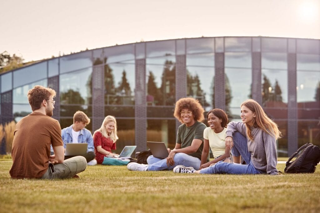 group of university or college students sit on grass outdoors on campus talking and working